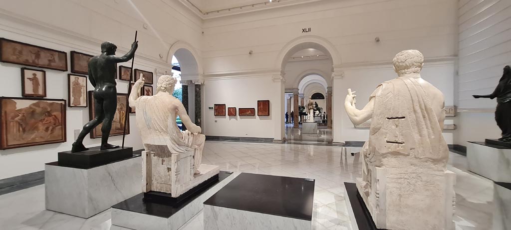 Herculaneum Augusteum. April 2023.
Looking across display from rear of statues in “Campania Romana” gallery in Naples Archaeological Museum towards paintings on left of Arch.
Photo courtesy of Giuseppe Ciaramella.
