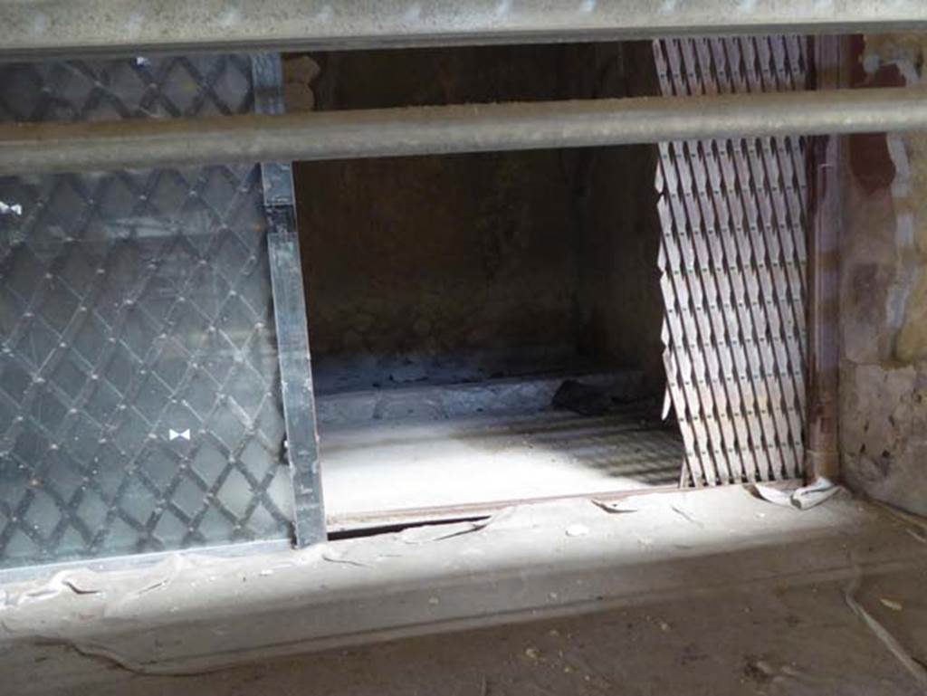 V.15 Herculaneum, September 2016. Detail of wooden sliding gate, separating the right (west) ala from the atrium.  Photo courtesy of Michael Binns.
According to Camardo and Notomista, an extraordinary carbonized wooden sliding gate was found in the right ala dividing it from the atrium, it was restored and left in situ. The gate was surmounted by a wooden cornice with a frieze in relief. On page 228 is a photo of the gate with detail of the wooden cornice with frieze. 
The photo was taken in the 1960s and shows that the right-hand side of the screen was reconstructed with modern wood after the damage reported from the bombing in April 1943.
See Camardo, D, and Notomista, M, eds. (2017). Ercolano: 1927-1961. Limpresa archeologico di Amedeo Maiuri e lesperimento della citta museo. Rome, LErma di Bretschneider, (p.227-8, Scheda 24).

