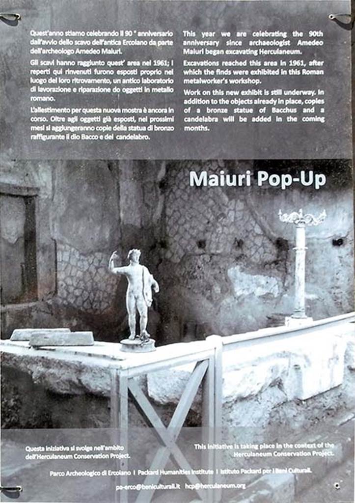 VI.12, Herculaneum. May 2018. Notice from front of shop.
“This year we celebrate the 90th anniversary since archaeologist Amedeo Maiuri began excavating Herculaneum.
Excavations reached this area in 1961, after which the finds were exhibited in this Roman metalworker’s workshop.
Work on this new exhibit is still underway. In addition to the objects already in place, copies of a bronze statue of Bacchus and a candelabra will be added in the coming months.”
Photo courtesy of Buzz Ferebee. 
(translation –
“Quest’anno stiamo celebrando il 90 anniversario dall avvio dello scavo dell’antica Ercolano da parte dell’archeologo Amedeo Maiuri. Gli scavi hanno raggiunto quest’area nel 1961; i reperti qui rinvenuti furono esposti proprio nel luogo del ritrovamento, un antico laboratorio di lavorazione e riparazione di oggetti in metallo romano.
L’allestimento per questa nuova mostra e ancora in corso. 
Oltri agli oggetti gia esposti, nel prossimi mesi si aggiungeranno copie della statua di bronzo raffigurante il dio Bacco e del candelabra.”).


