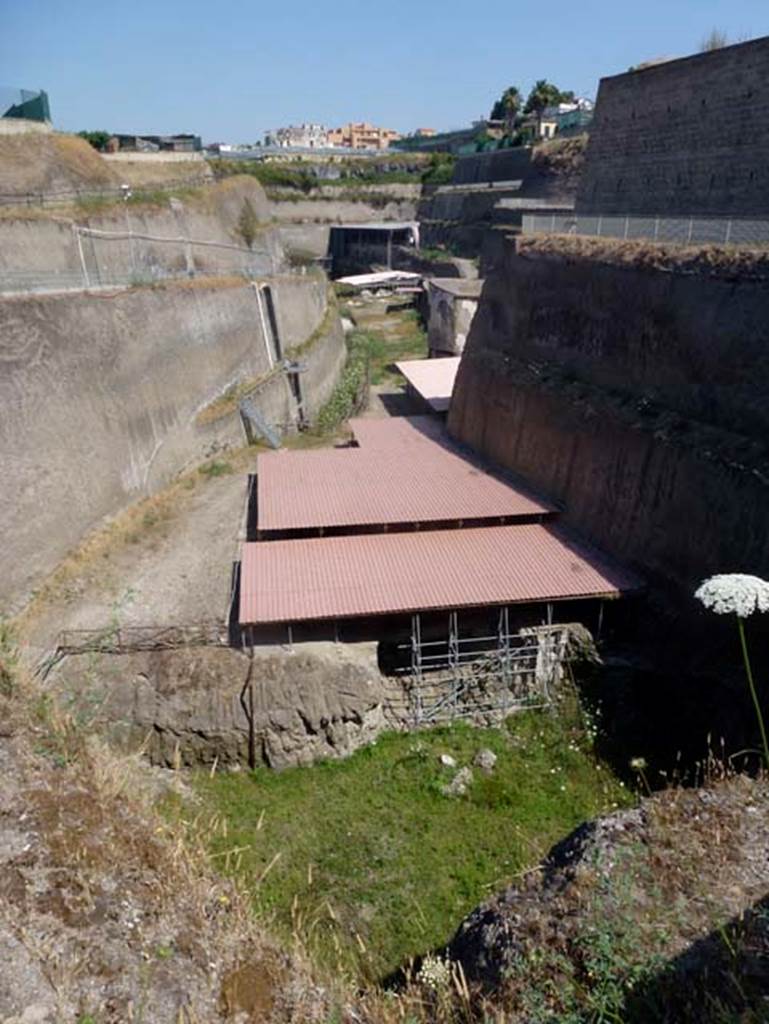 Villa dei Papiri complex, June 2014. Overview of site, looking west.
Photo courtesy of Michael Binns.
From front to back are:
The double roof of the House of the Dionysiac Reliefs, seaside pavilion.     
The paler coloured roof around the corner is the House of the Dionysiac Reliefs.
The tall building of the baths.
The white roof covering the collapsed monumental structure.
The levels of the Villa dei Papiri itself.

