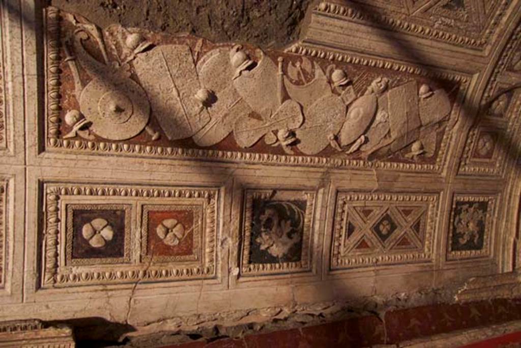 Villa dei Papiri, Herculaneum. July 2010. Room (I) on lower terrace, east side of vaulted stucco ceiling with frieze showing a pile of weapons. Photo courtesy of Michael Binns.
The weapons are represented with extreme accuracy in white stucco on a red background. 
The weapons are predominantly north European, but the are also Hellenistic, eastern and barbarian weapons. Defensive weapons include a breastplate with corset, two greaves, nine helmets and fourteen shields of different shapes and sizes including a rare figure of eight shield with two concavities. The shields have incised decorations realized with a stylus.
Offensive weapons include a two-edged axe, a gorytos (quiver) with a sheaf of arrows, two swords, a makhaira (curved sword) and three spears.
See Esposito D. and Guidobaldi M., 2010. New Archaeological Research at the Villa of the Papyri, in the Villa of the Papyri at Herculaneum. Berlin: De Gruyter, p. 38-9. 


