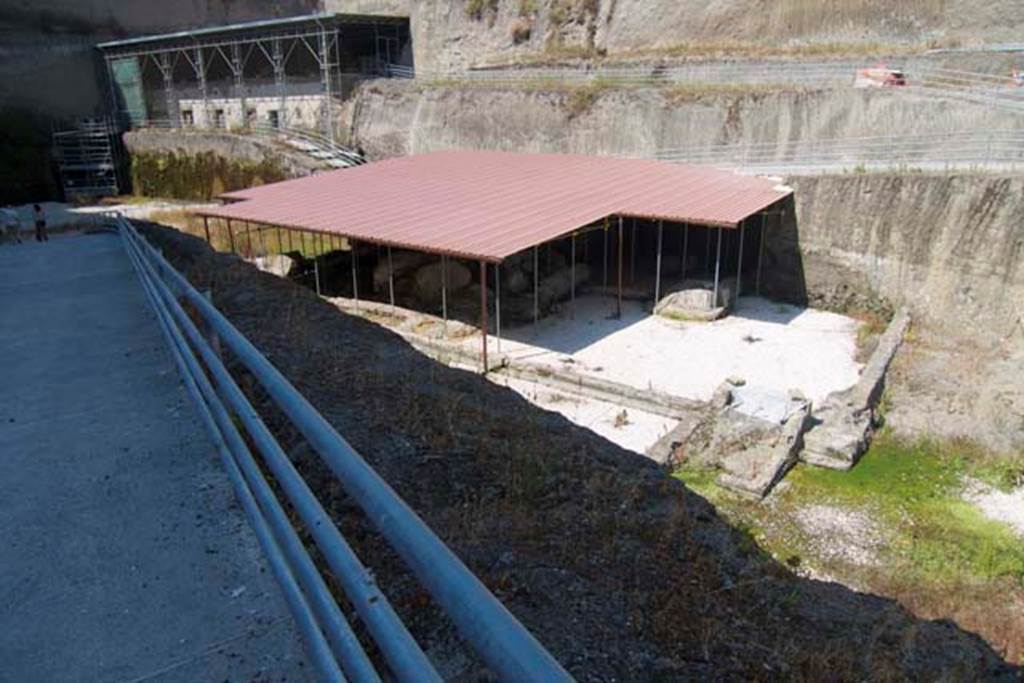 Villa dei Papiri, Herculaneum. July 2010. 
Looking north-west towards area of collapsed “large or monumental structure”, possibly coinciding with the western entrance of the villa overlooking the sea.  Photo courtesy of Michael Binns.
At the front of the structure is a rectangular pool parallel to the ancient coastline (the white shadowed area at the front centre in this photo).
A room of uncertain function juts out along the side of the pool. To the side of this room is a small stairway and ramp leading to the ancient beach.
See Guidobaldi, M. P. The Ivory Tripods. (p.114-5 of Buried by Vesuvius, the Villa dei Papiri at Herculaneum, edited by Kenneth Lapatin).
According to Camardo –
“The most important achievement of the open-air excavation (of 1996) was the discovery of the monumental structure with the same orientation as the Villa but situated on a large terrace some ten metres below its piano nobile, and jutting out noticeably farther towards the sea. 
This was only partially unearthed because it had completely collapsed under the weight of the pyroclastic debris that had buried it. 
The collapsed part was recovered whole, since the structure had not been cut into by the Bourbon-era tunnels. 
A monumental hall (see fig. d in plan (14.1) on p.114) is fairly well preserved: a series of brick pilasters covered in stucco supported a set of large wooden beams with a flat ceiling in opus signinum (tiny broken tiles mixed with mortar). 
A white marble threshold graced the broad entrance of the seaward side of the building.”
See Camardo, D. Recent excavations in the Villa dei Papiri 1990’s – 2008. (p.105-113 of Buried by Vesuvius, the Villa dei Papiri at Herculaneum, edited by Kenneth Lapatin).
