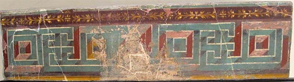 Villa dei Papiri, Herculaneum. Atrium (c). Meander fresco.
Now in Naples Archaeological Museum. Inventory number 8548.
According to Esposito, the upper part of the atrium's walls was decorated with a perspective meandering frieze, of which a fragment was recovered during the eighteenth-century explorations. 
The relevance of this piece to the decoration of the atrium, for a long time discussed, can now be confirmed by the discovery of a small fragment of painted plaster that exhibits a purple bottom band, next to which is painted a green band and adorned with a stylized floral element with eight petals, fielded in orange with cream white highlights. 
The motive of the perspective meander is very frequent in the pavement and parietal decorations of the late Republican age. In particular it is often used as a frieze placed to crown the median area.
See Esposito D., 2010. Le pitture della Villa dei Papiri ad Ercolano in La Villa Romaine de Boscoreale et ses Fresques. Édicions errance: Musée royal de Mariemont. p. 214, fig. 6.
